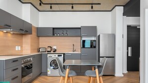 A modern kitchen with grey cabinets, a built-in oven, a microwave, and a refrigerator. There is a washing machine and a table with two chairs. - Bridgewater One  | Netflix | Fibre (Cape Town)