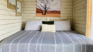 A room with a bed, a painting of a tree on the wall, and a window with blinds. - The Indigo House at Canyon Lake (Canyon Lake)