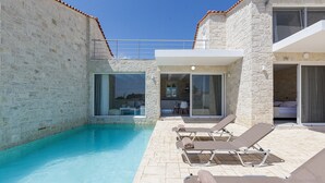 A poolside area with lounge chairs, a stone wall, and a glass door leading to a room.