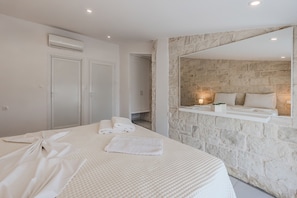 Een hotelkamer met een bed, een stenen muur, een spiegel en een klein plankje met een plant.