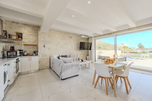 A modern living space with a kitchen, dining area, and a large window offering a view of the outdoors. - Mythos villa III,pool,Walking distance to beach (Damnoni)