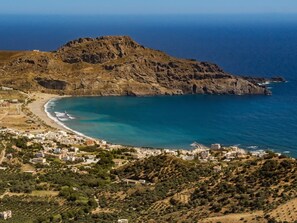 A coastal town with a beach, rocky hills, and a clear view of the sea.