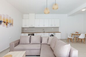 Una sala de estar moderna con un sofá, una mesa de comedor con sillas y una zona de cocina con armarios y una lavadora.