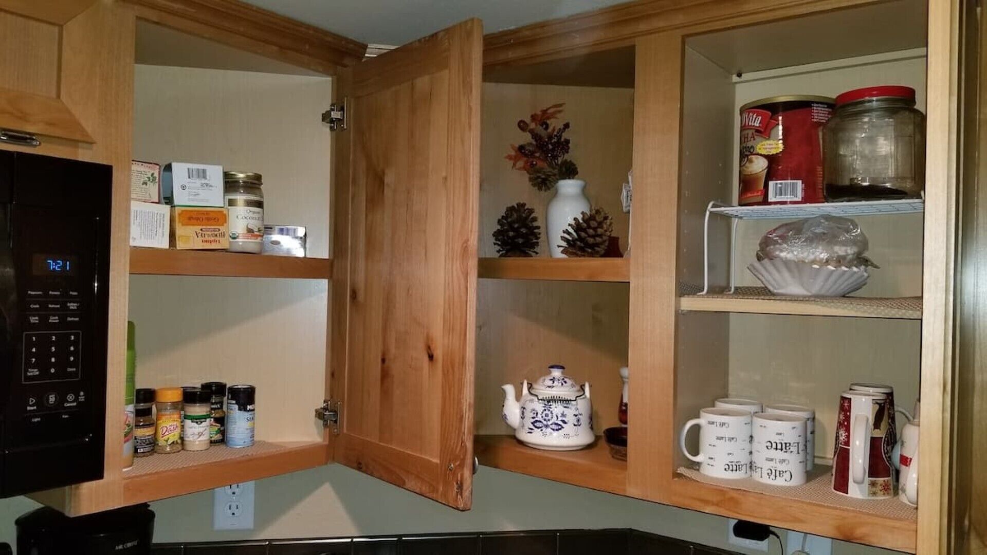 A kitchen with wooden cabinets, a microwave, and various kitchen items on shelves.
