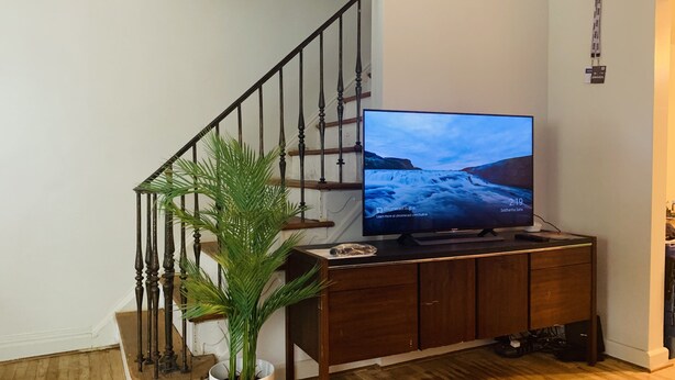 A living room with a wooden staircase, a television on a wooden cabinet, and a potted plant. - Private Queen Bedroom Garvin (Sharon Hill)