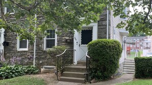 A stone building with a front door, steps, and a small garden with plants and a pathway. - Private Queen Bedroom Garvin (Sharon Hill)
