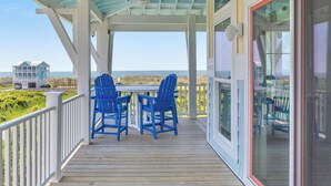 Un espace extérieur abrité, équipé d’une table et de deux chaises, d’où l’on a vue sur une plage et une maison.