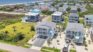Un quartier résidentiel en bord de mer, avec des maisons modernes à deux étages, une plage en arrière-plan et un ciel dégagé.