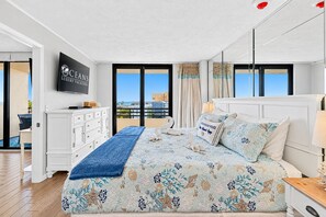 A hotel room with a large bed, a TV on the wall, and a view of the city through the windows.