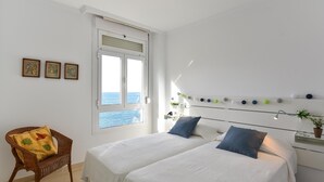 Une chambre avec deux lits, un fauteuil en osier, une fenêtre donnant sur un paysage agréable et des décorations murales.
