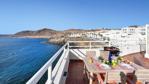 Une terrasse avec une table dressée pour le dîner, offrant une vue sur une ville côtière et la mer.