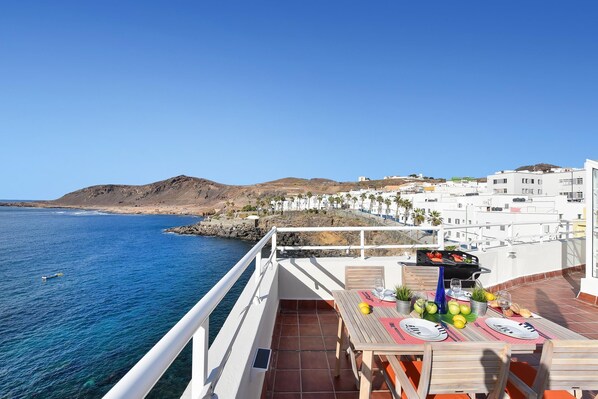A terrace with a table set for dining, overlooking a coastal town and the sea.