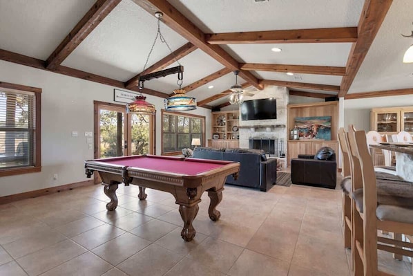 A pool table in a room with wooden beams, a fireplace, and a television.