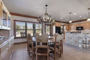 A spacious kitchen with a dining area, wooden cabinets, a stone island, and a chandelier.