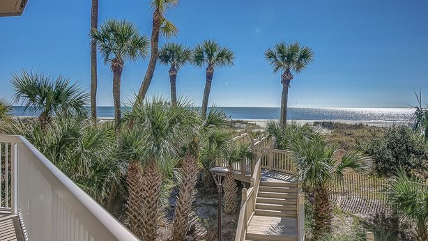 A staircase leading to a balcony overlooking a beach with palm trees and a clear blue sky. - Enjoy the Large Wrap Around Ocean Front Balcony! (Hilton Head Island)