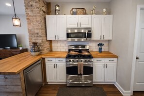 A kitchen with white cabinets, a stainless steel stove, a microwave, and a brick wall.