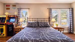 Ein Schlafzimmer mit einem großen Bett, zwei Nachttischen, Spielautomaten und einem Fenster mit gemusterten Vorhängen.