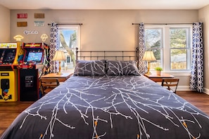 Ein Schlafzimmer mit einem großen Bett, zwei Nachttischen, Spielautomaten und einem Fenster mit gemusterten Vorhängen.