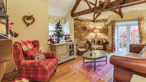 A cozy living room with a plaid sofa, a leather armchair, a wooden ceiling, a stone wall, a Christmas tree, and a fireplace. - 2 bedroom accommodation in Felton (Felton)