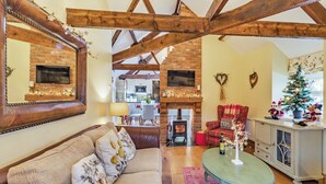 A cozy living room with a fireplace, a sofa, a dining table, and a kitchen in the background. - 2 bedroom accommodation in Felton (Felton)