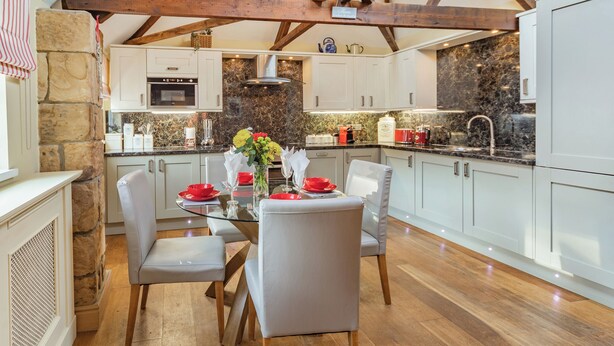 A modern kitchen with white cabinets, a stone accent wall, and a dining area with a glass table and chairs. - 2 bedroom accommodation in Felton (Felton)