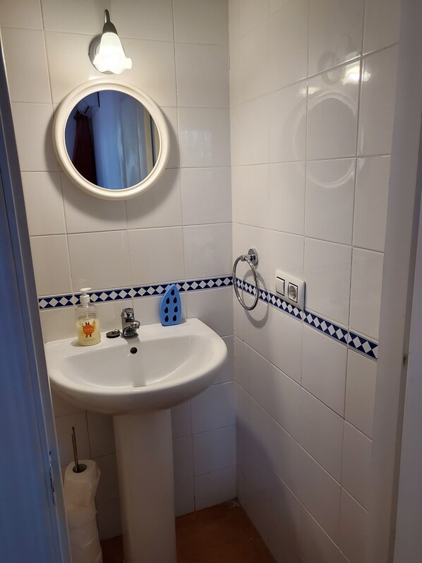 A bathroom with a white sink, a mirror, a blue and white tiled backsplash, a towel rack, and a toilet paper holder.