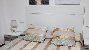 Una cama bien tendida con ropa de cama a rayas y dos almohadas, una mesita de noche con una lámpara y dos cuadros en la pared sobre la cama.