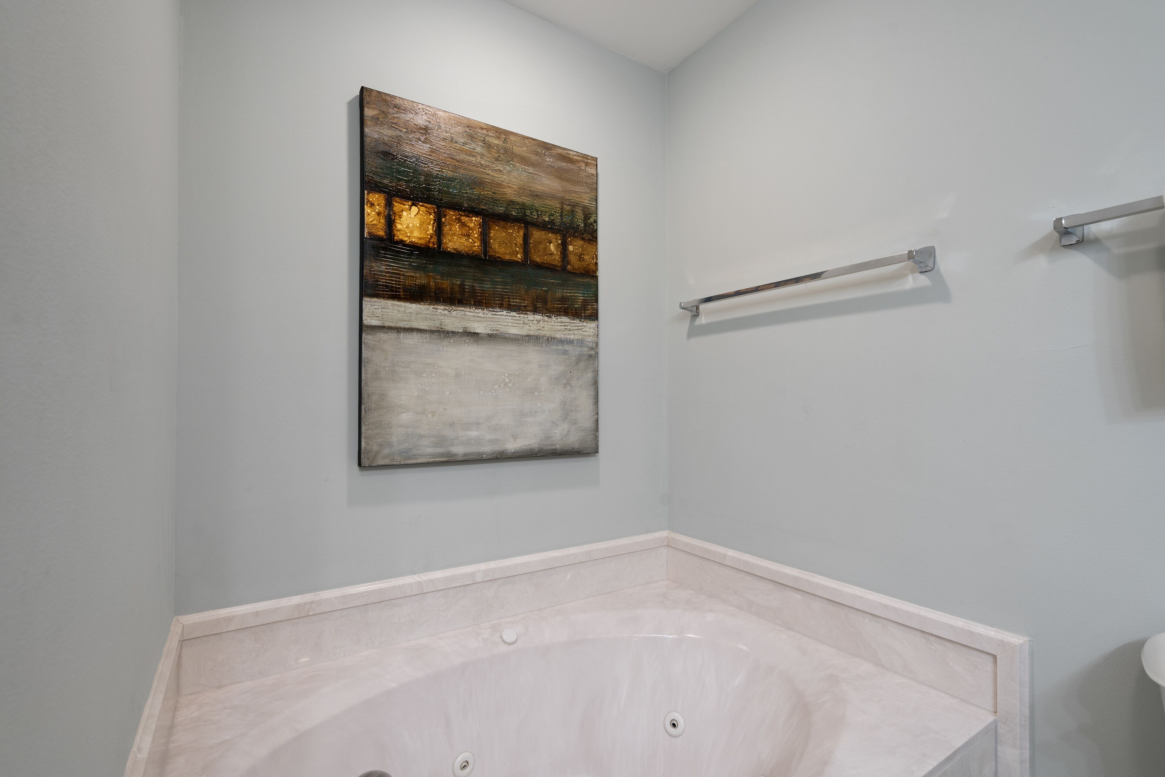 A bathroom with a marble bathtub, a towel rack, and a wall-mounted abstract painting.