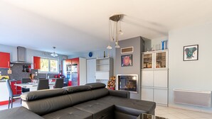 A modern kitchen with red cabinets, a dining area with a black leather sofa, and a living room with a glass coffee table. - Gawa's House - Maison avec jardin proche mer (Meschers-sur-Gironde)
