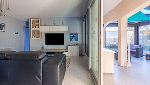 A modern living room with a flat-screen TV, a sofa, a small cabinet, and a dining area with a table and chairs. - Gawa's House - Maison avec jardin proche mer (Meschers-sur-Gironde)