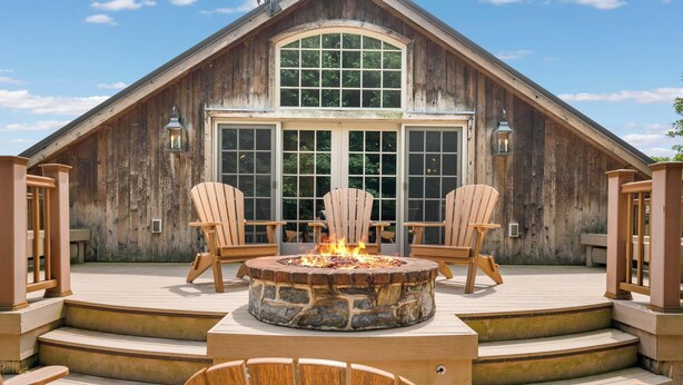 Un bâtiment en bois avec un foyer en pierre et deux fauteuils Adirondack devant.