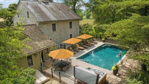 Une maison en pierre avec une piscine, un espace salon extérieur et un jacuzzi.
