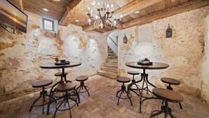 Un intérieur rustique avec des poutres apparentes, un lustre et plusieurs tables rondes accompagnées de tabourets.