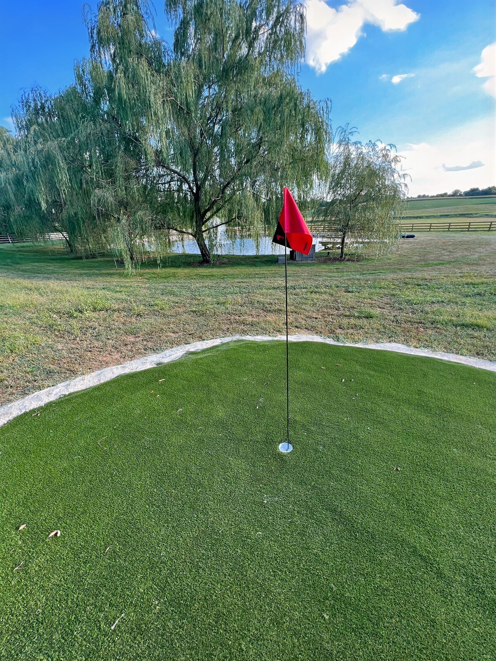 Un campo de golf con una bandera roja que marca el hoyo, rodeado de césped cuidado y árboles.