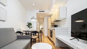 Une cuisine moderne avec des meubles blancs, un plan de travail en bois et un coin repas comprenant un canapé gris et une table ronde.