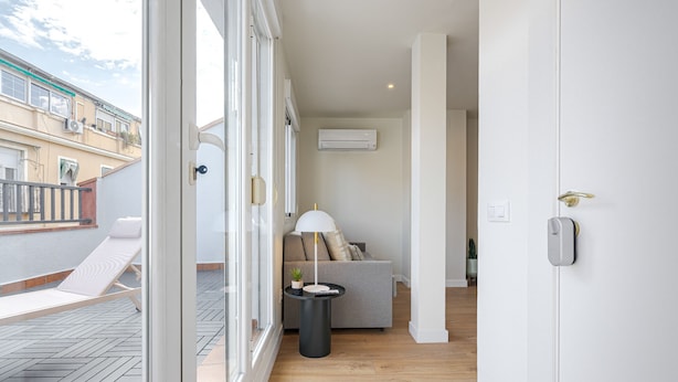 Un salon moderne avec un canapé, une petite table et une lampe, ainsi qu’un balcon équipé d’une chaise longue.