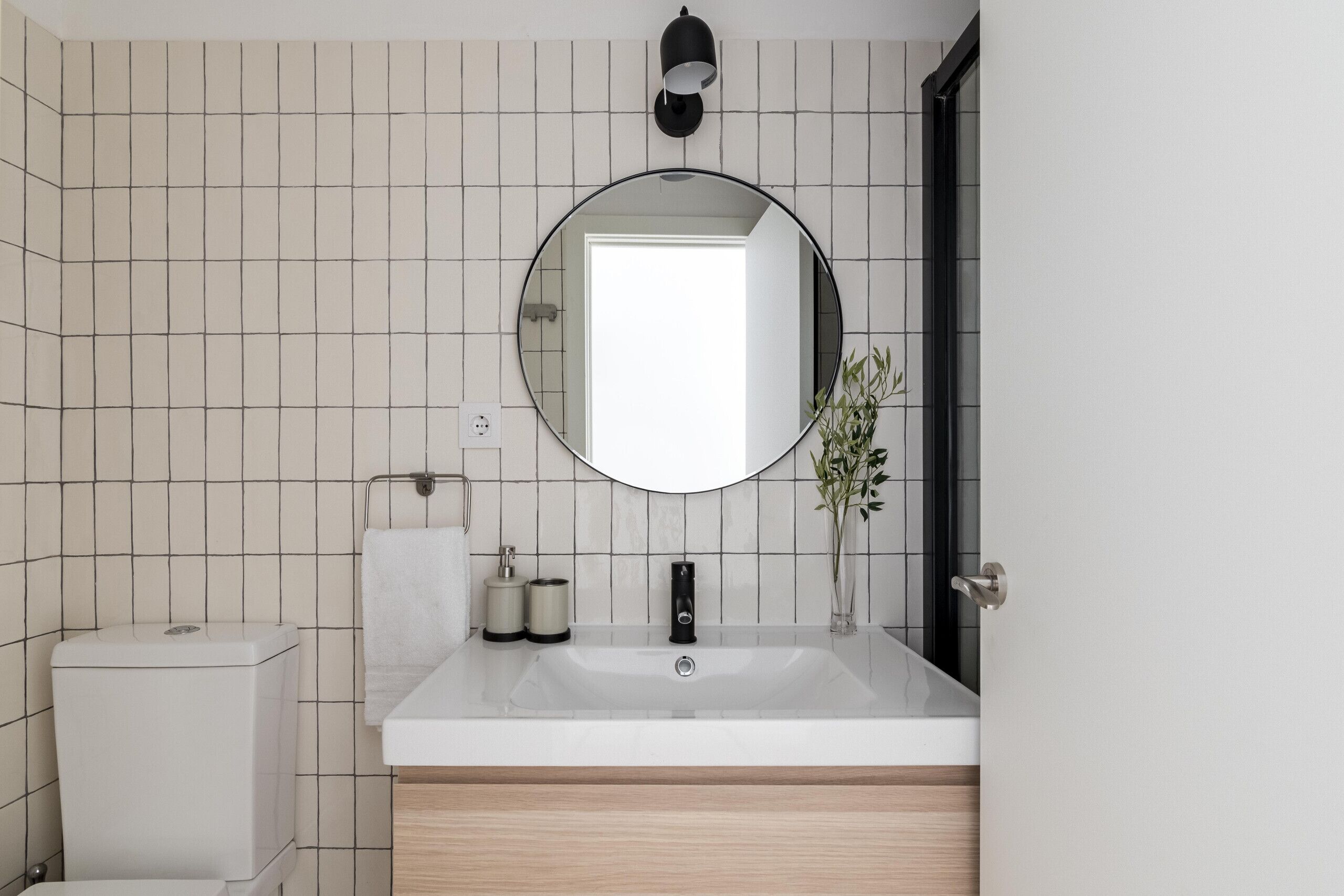 Un bagno moderno con un lavandino bianco, uno specchio rotondo e un water.