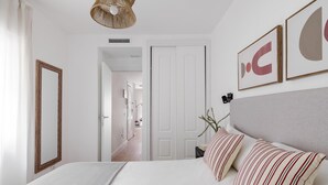 Une chambre à coucher comprenant un lit, une table de chevet, un miroir et une porte donnant sur une autre pièce.