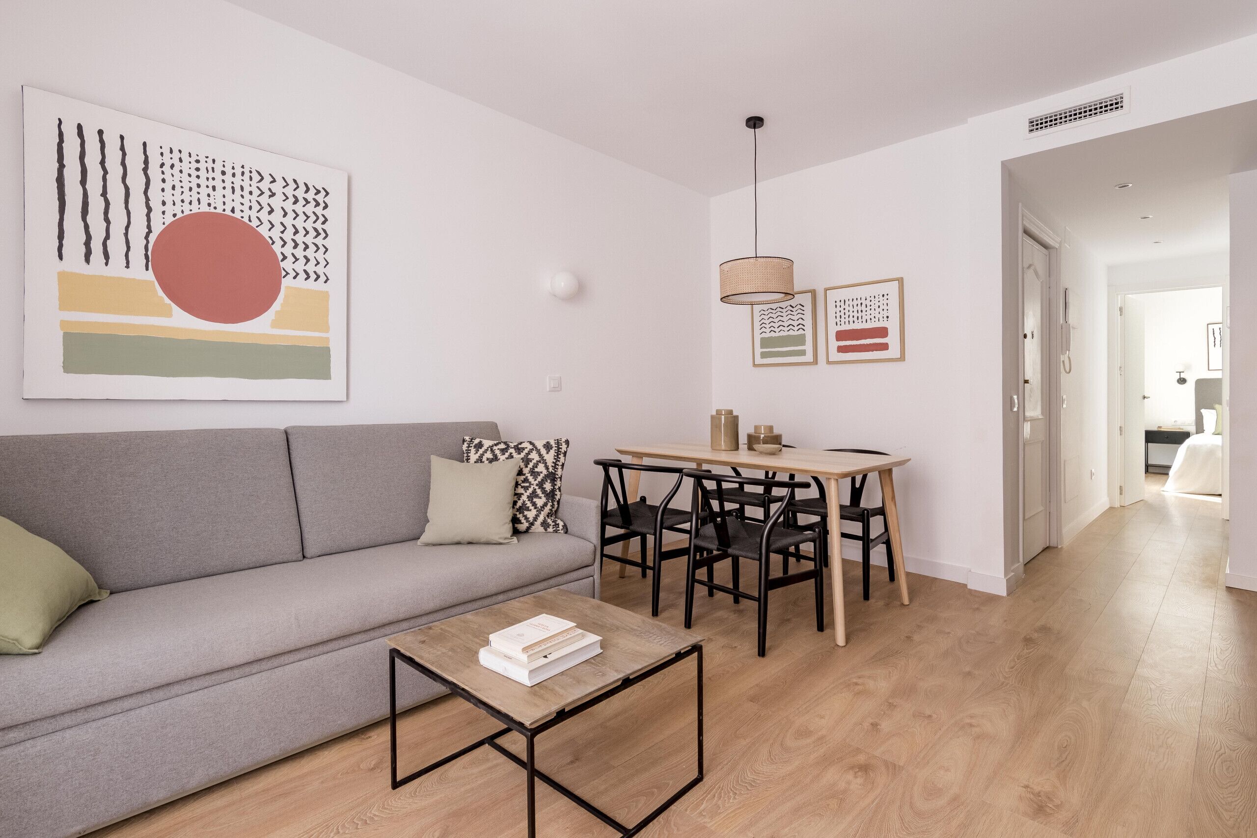 A modern living room with a grey sofa, a wooden coffee table, and a dining area with a table and chairs.