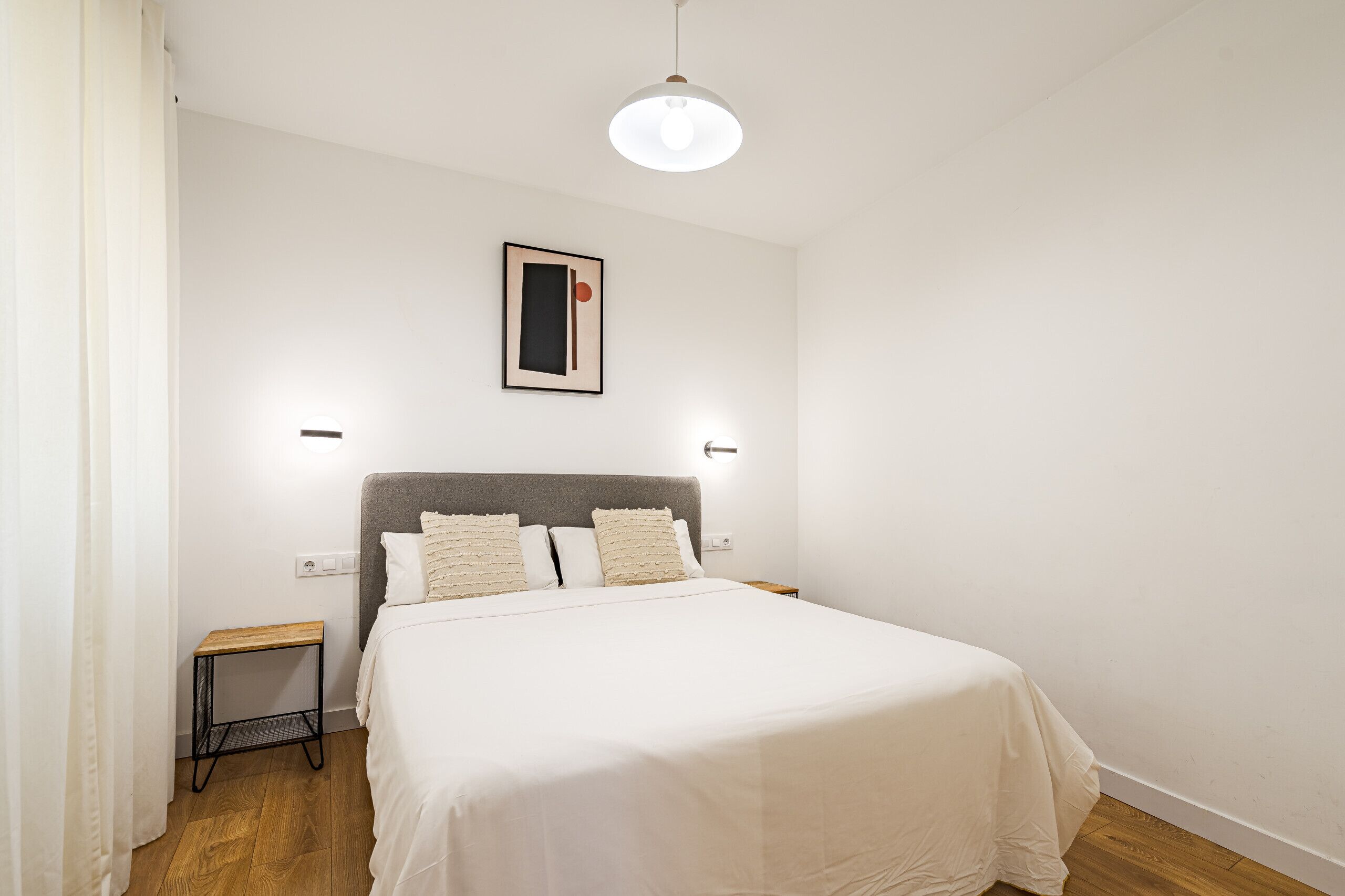 Ein ordentlich eingerichtetes Schlafzimmer mit einem Bett, Nachttischen, einer Hängelampe und einem gerahmten Bild an der Wand.