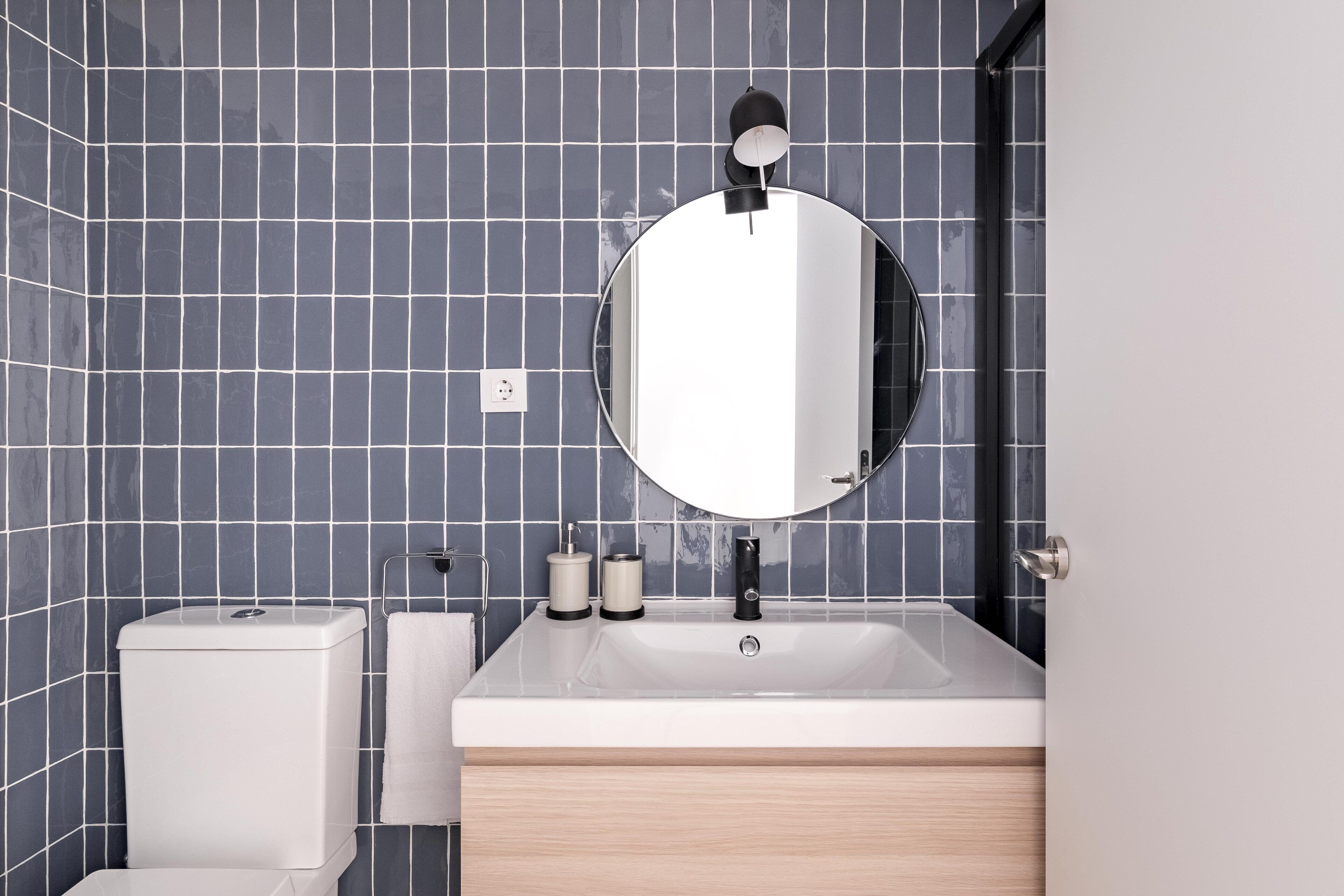 Une salle de bain moderne avec un lavabo blanc, un miroir rond et des toilettes.