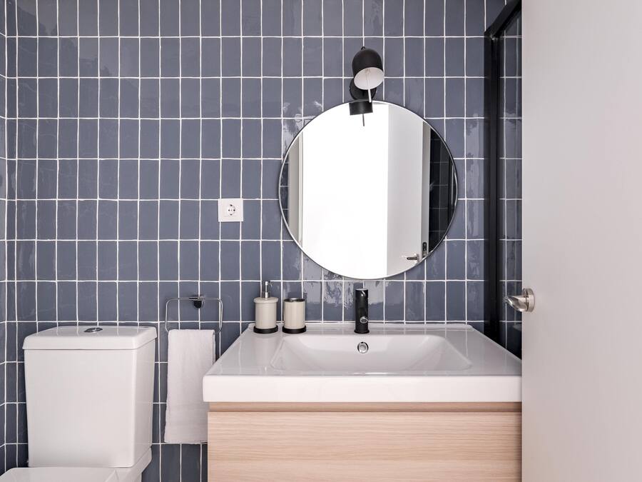 A modern bathroom with a white sink, a round mirror, and a toilet.