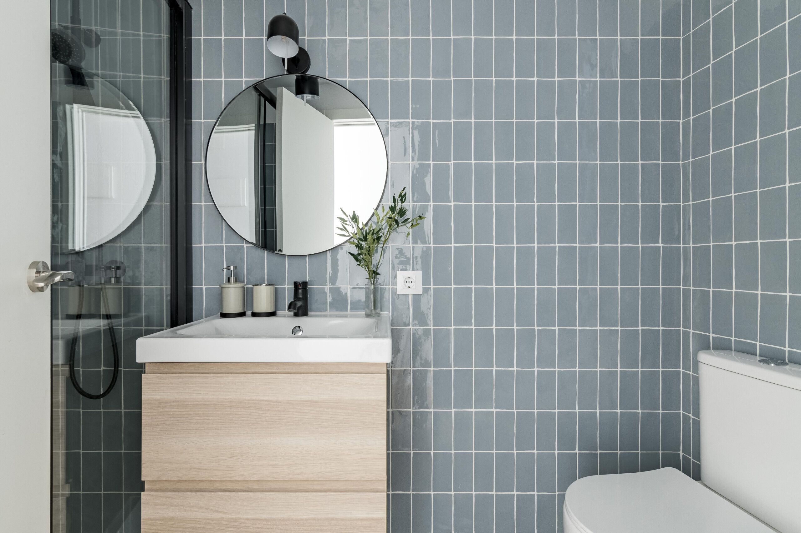 A modern bathroom with a white sink, two round mirrors, a black light fixture, and a toilet.