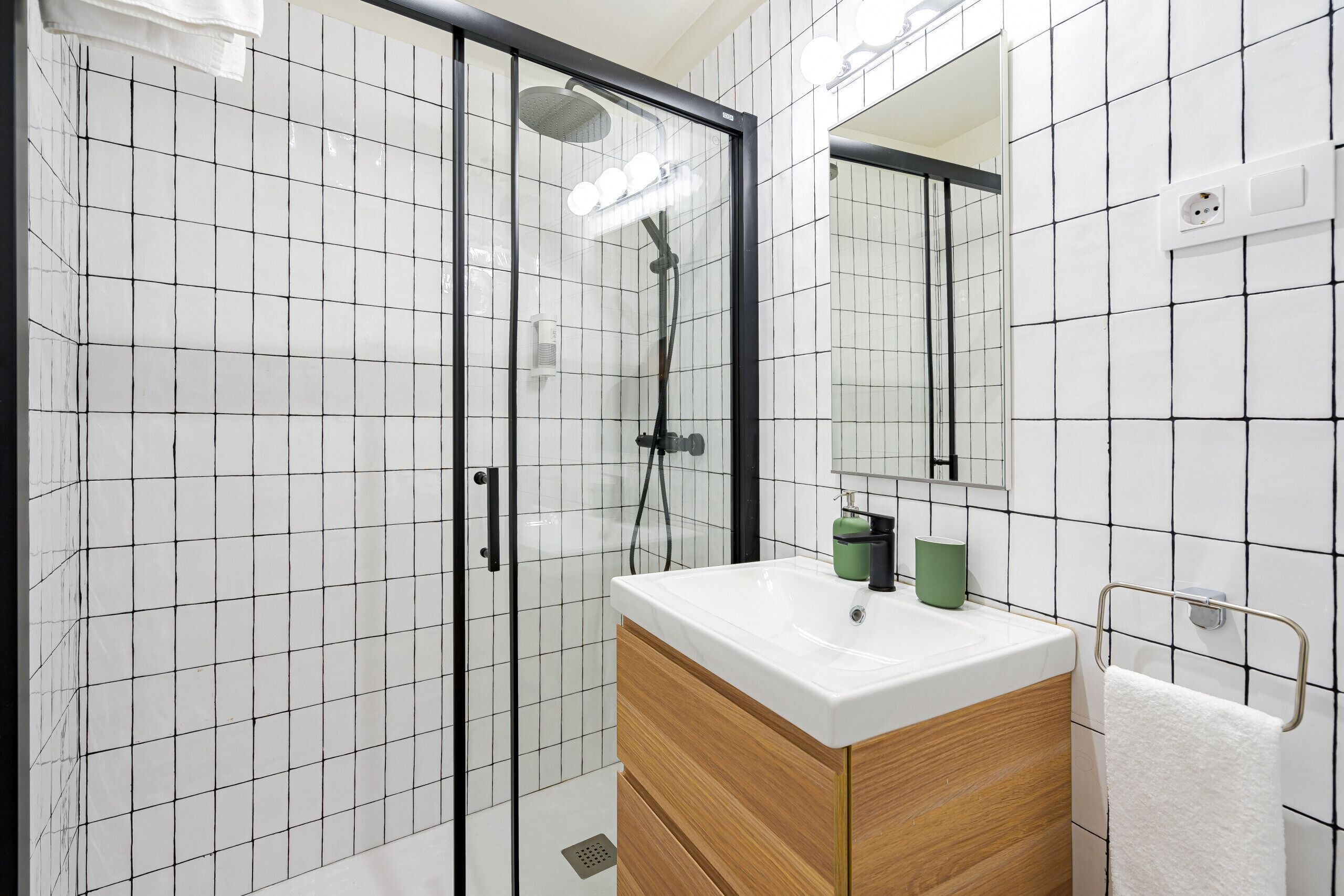 A modern bathroom with a glass-enclosed shower, a white sink with a wooden vanity, and a mirror above the sink.
