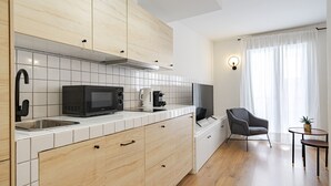 Une cuisine moderne avec des meubles blancs, un four à micro-ondes, une machine à café et un évier. On y trouve une chaise noire et une petite table avec une plante.