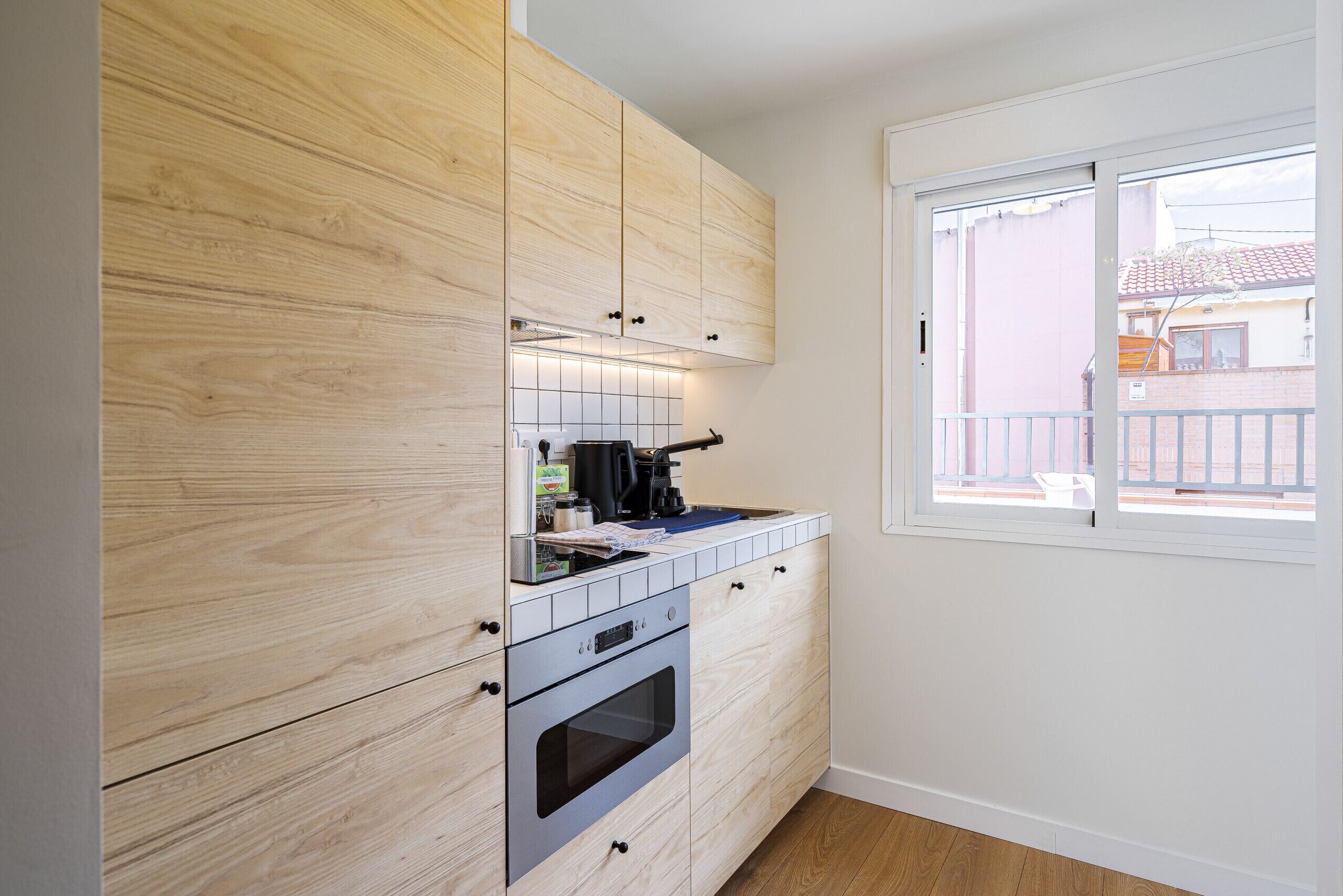 Una cocina compacta con armarios de madera, horno empotrado y ventana que proporciona luz natural.