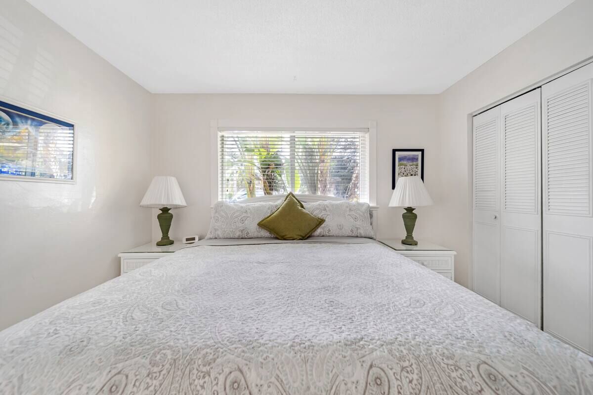 Quarto com cama grande, duas mesas de cabeceira, janela com persianas e guarda-roupa.
