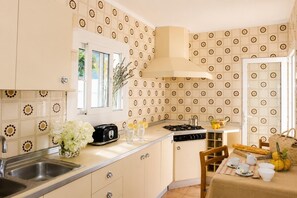 A kitchen with a window, a toaster, a sink, and a dining area with a table set for two. - Villa Roca Nova - Four Bedroom Villa, Sleeps 8 (Cala d'Or)