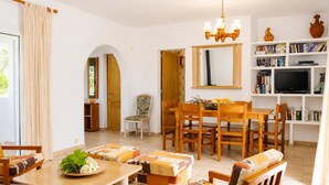 A living room with a dining table, chairs, a sofa, a bookshelf, a television, and a mirror. - Villa Roca Nova - Four Bedroom Villa, Sleeps 8 (Cala d'Or)
