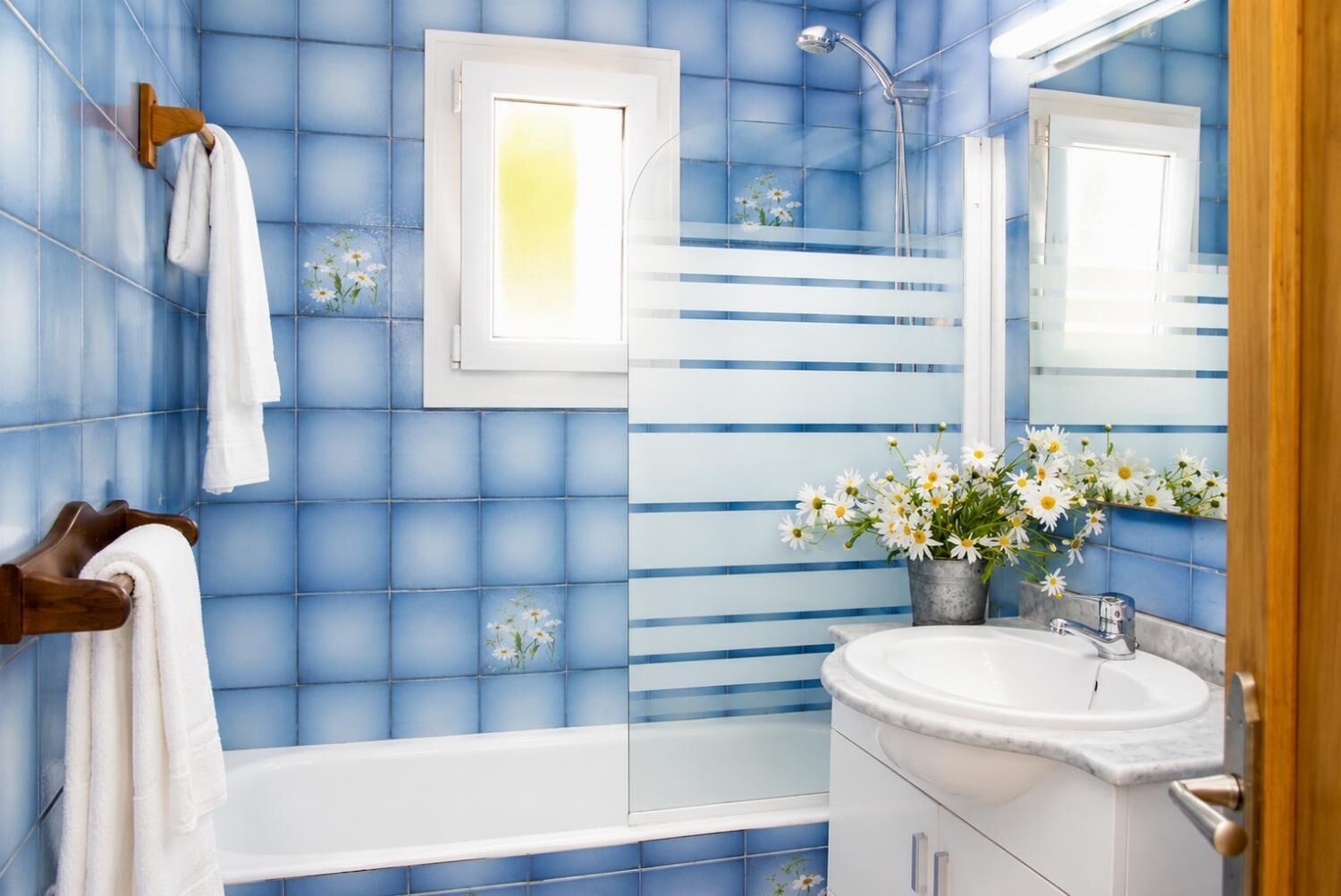 A bathroom with blue tiles, a white bathtub, a sink with a mirror, and a towel rack.